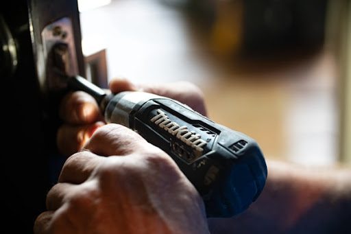 A cordless electric drill being used on a door lock.