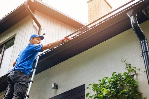 A contractor on a ladder cleans a home's gutters.